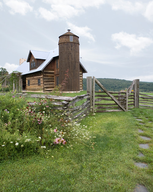 A beautiful farmhouse with a silo framed by a rustic split rail fence, a wealth of wildflowers, and a flagstone path leading up to it.