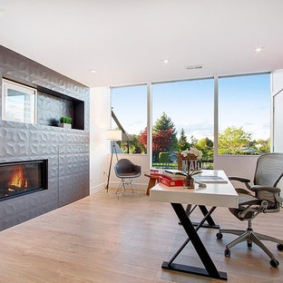 This is an example of a large modern study in Seattle with grey walls, dark hardwood flooring, a standard fireplace, a tiled fireplace surround, a freestanding desk and brown floors.