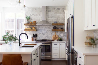 Transitional l-shaped laminate floor and brown floor kitchen photo in Los Angeles with an undermount sink, shaker cabinets, white cabinets, quartz countertops, gray backsplash, marble backsplash, stainless steel appliances and an island
