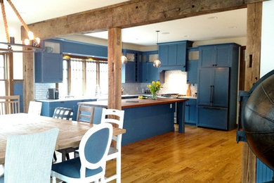 Inspiration for a large coastal l-shaped medium tone wood floor open concept kitchen remodel in Boston with a farmhouse sink, shaker cabinets, blue cabinets, wood countertops, blue backsplash, subway tile backsplash, paneled appliances and an island