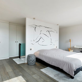 Aménagement d'une grande chambre parentale contemporaine avec un mur blanc, un sol en bois brun et un sol gris.