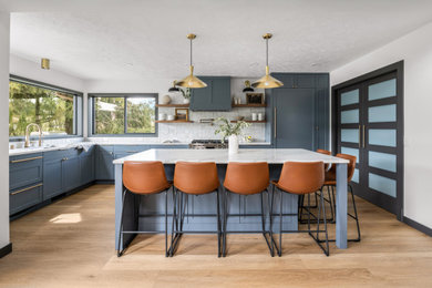 Eat-in kitchen - mid-sized transitional l-shaped eat-in kitchen idea in Seattle with a single-bowl sink, shaker cabinets, blue cabinets, solid surface countertops, white backsplash, paneled appliances, an island and white countertops