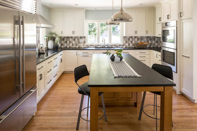 This is an example of a mid-sized transitional u-shaped kitchen in Minneapolis with an undermount sink, recessed-panel cabinets, white cabinets, granite benchtops, multi-coloured splashback, ceramic splashback, stainless steel appliances, medium hardwood floors, with island and brown floor.