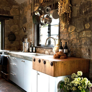 На фото: маленькая линейная кухня-гостиная в стиле рустика с монолитной раковиной, плоскими фасадами, фасадами из нержавеющей стали, столешницей из бетона, бетонным полом, островом, бежевым фартуком и техникой из нержавеющей стали с