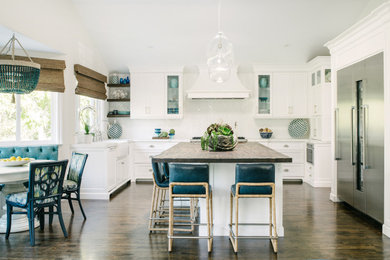 Photo of a large beach style l-shaped eat-in kitchen in Los Angeles with a farmhouse sink, shaker cabinets, white cabinets, solid surface benchtops, white splashback, ceramic splashback, stainless steel appliances, dark hardwood floors, with island, brown floor and white benchtop.