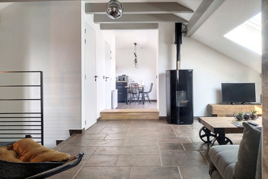 Imagen de sala de estar abierta contemporánea con paredes blancas, suelo de baldosas de cerámica, estufa de leña, televisor independiente, suelo marrón y vigas vistas