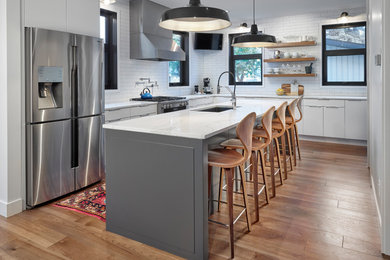 Mid-sized l-shaped eat-in kitchen in Edmonton with a double-bowl sink, flat-panel cabinets, white cabinets, quartz benchtops, white splashback, subway tile splashback, stainless steel appliances, light hardwood floors, with island, beige floor and white benchtop.