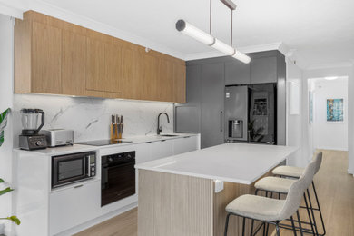 Design ideas for a large modern galley kitchen pantry in Gold Coast - Tweed with an undermount sink, flat-panel cabinets, quartz benchtops, white splashback, engineered quartz splashback, black appliances, vinyl floors, with island, beige floor, white benchtop and recessed.