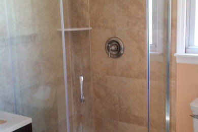 Inspiration for a mid-sized transitional 3/4 beige tile and ceramic tile ceramic tile and beige floor corner shower remodel in New York with raised-panel cabinets, black cabinets, a two-piece toilet, beige walls, an undermount sink, solid surface countertops and a hinged shower door
