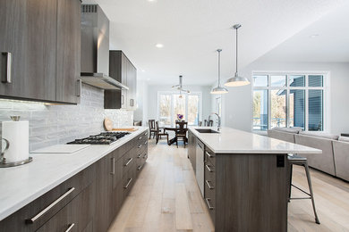 This is an example of a mid-sized modern open plan kitchen in Edmonton with an undermount sink, flat-panel cabinets, grey cabinets, quartz benchtops, white splashback, ceramic splashback, stainless steel appliances, light hardwood floors, with island, brown floor and white benchtop.