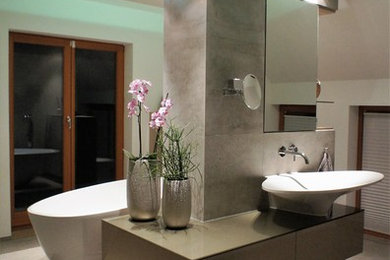 Mittelgroßes Modernes Badezimmer mit Glasfronten, braunen Schränken, freistehender Badewanne, bodengleicher Dusche, Wandtoilette, grauen Fliesen, Steinfliesen, brauner Wandfarbe, Aufsatzwaschbecken, Glaswaschbecken/Glaswaschtisch und Keramikboden in Leipzig