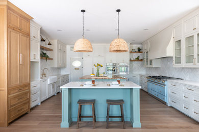 Inspiration for a mid-sized country u-shaped light wood floor and brown floor enclosed kitchen remodel in Dallas with a farmhouse sink, shaker cabinets, white cabinets, quartz countertops, white backsplash, ceramic backsplash, stainless steel appliances, two islands and white countertops