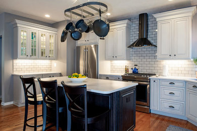 Example of a mid-sized transitional l-shaped medium tone wood floor and red floor eat-in kitchen design in Other with an undermount sink, raised-panel cabinets, gray cabinets, quartz countertops, gray backsplash, subway tile backsplash, stainless steel appliances, an island and white countertops