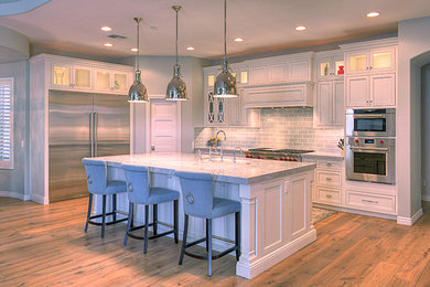 Inspiration for a large transitional l-shaped medium tone wood floor kitchen remodel in Phoenix with an undermount sink, recessed-panel cabinets, white cabinets, gray backsplash, subway tile backsplash, stainless steel appliances and an island