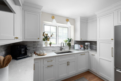 Eat-in kitchen - mid-sized traditional u-shaped medium tone wood floor and brown floor eat-in kitchen idea in Chicago with a single-bowl sink, flat-panel cabinets, white cabinets, quartz countertops, gray backsplash, ceramic backsplash, stainless steel appliances, a peninsula and gray countertops