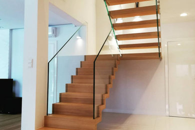 Foto de escalera en U de tamaño medio con escalones de madera, contrahuellas de madera y barandilla de vidrio