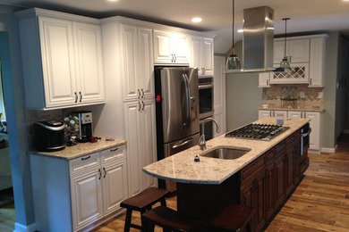 Photo of a large transitional l-shaped separate kitchen in Philadelphia with an undermount sink, raised-panel cabinets, white cabinets, granite benchtops, beige splashback, stone tile splashback, stainless steel appliances, porcelain floors, with island and brown floor.