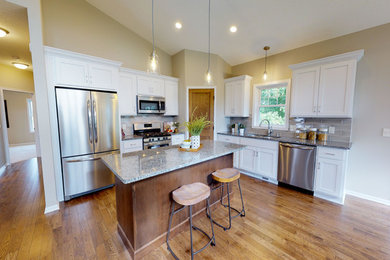 Inspiration for a mid-sized timeless u-shaped medium tone wood floor and brown floor eat-in kitchen remodel in Minneapolis with an undermount sink, recessed-panel cabinets, white cabinets, granite countertops, gray backsplash, subway tile backsplash, stainless steel appliances, an island and multicolored countertops