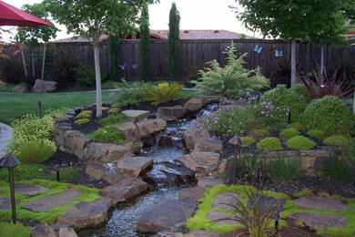 Photo of a large mediterranean backyard full sun garden for summer in Sacramento with a water feature and natural stone pavers.