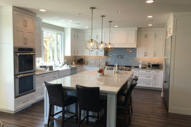 Example of a large farmhouse u-shaped dark wood floor and brown floor eat-in kitchen design in Orange County with a farmhouse sink, shaker cabinets, white cabinets, marble countertops, gray backsplash, subway tile backsplash, stainless steel appliances, an island and white countertops