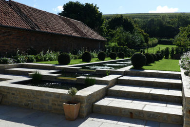 Large contemporary back formal full sun garden in Wiltshire with a waterfall and natural stone paving.