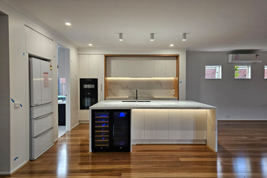 Photo of an open plan kitchen in Melbourne with an undermount sink, white cabinets, marble benchtops, marble splashback, black appliances, light hardwood floors and with island.