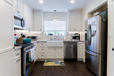This is an example of a mid-sized transitional u-shaped eat-in kitchen in Los Angeles with a farmhouse sink, recessed-panel cabinets, white cabinets, granite benchtops, white splashback, subway tile splashback, stainless steel appliances, dark hardwood floors, no island and brown floor.