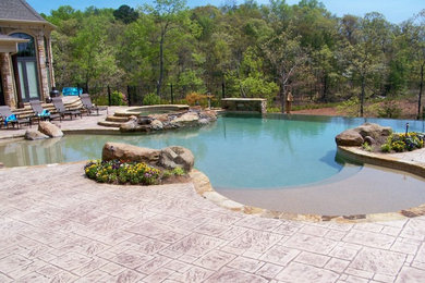Exemple d'une très grande piscine à débordement et arrière sur mesure avec un bain bouillonnant et du béton estampé.