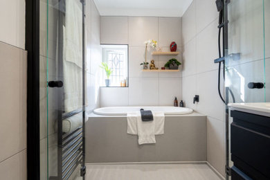 Photo of a medium sized contemporary grey and black family bathroom in Other with flat-panel cabinets, black cabinets, a built-in bath, a walk-in shower, a wall mounted toilet, grey tiles, ceramic tiles, ceramic flooring, an integrated sink, quartz worktops, grey floors, a hinged door, grey worktops, feature lighting, a single sink and a floating vanity unit.