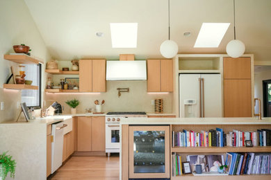 Example of a trendy light wood floor and vaulted ceiling kitchen design in Seattle with a farmhouse sink, light wood cabinets, white backsplash, white appliances, an island and white countertops