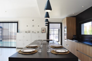 This is an example of a large contemporary galley eat-in kitchen in Marseille with an undermount sink, light wood cabinets, granite benchtops, black splashback, stone tile splashback, stainless steel appliances, concrete floors and with island.