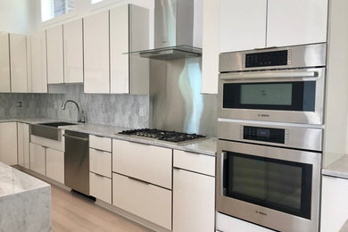 Inspiration for a large contemporary light wood floor kitchen remodel in New Orleans with a farmhouse sink, flat-panel cabinets, white cabinets, marble countertops, gray backsplash, marble backsplash, stainless steel appliances and an island