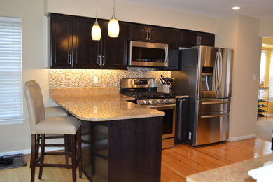 Inspiration for a small transitional u-shaped light wood floor and beige floor enclosed kitchen remodel in DC Metro with an undermount sink, shaker cabinets, dark wood cabinets, granite countertops, beige backsplash, glass sheet backsplash, stainless steel appliances, an island and beige countertops