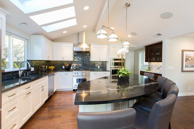 Large trendy l-shaped medium tone wood floor open concept kitchen photo in San Francisco with a double-bowl sink, shaker cabinets, white cabinets, granite countertops, black backsplash, subway tile backsplash, stainless steel appliances and an island