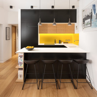 Foto di una piccola cucina ad U design con lavello sottopiano, ante lisce, ante nere, paraspruzzi giallo, parquet chiaro, penisola, pavimento marrone e elettrodomestici da incasso