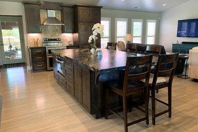 Photo of a large traditional l-shaped open plan kitchen in Sacramento with an undermount sink, shaker cabinets, dark wood cabinets, beige splashback, stone tile splashback, stainless steel appliances, light hardwood floors, with island, beige floor and black benchtop.