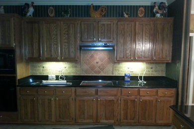 Modelo de cocina tradicional pequeña cerrada con fregadero bajoencimera, armarios con paneles empotrados, puertas de armario de madera oscura, encimera de granito, salpicadero marrón y salpicadero de azulejos de piedra