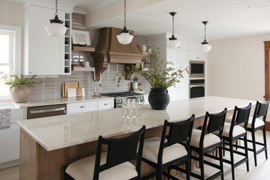 Large transitional l-shaped light wood floor and beige floor eat-in kitchen photo in Other with a farmhouse sink, recessed-panel cabinets, white cabinets, quartz countertops, beige backsplash, subway tile backsplash, stainless steel appliances, an island and beige countertops