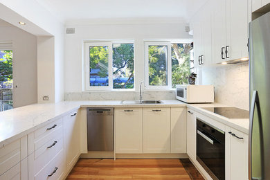 Inspiration for a mid-sized traditional u-shaped eat-in kitchen in Sydney with a drop-in sink, shaker cabinets, white cabinets, quartz benchtops, white splashback, stone slab splashback, stainless steel appliances, plywood floors, yellow floor and white benchtop.