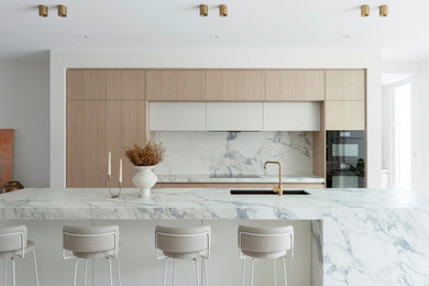 Inspiration for a modern galley kitchen in Perth with an undermount sink, flat-panel cabinets, light wood cabinets, white splashback, stone slab splashback, black appliances, with island and white benchtop.
