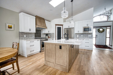 Inspiration for a mid-sized craftsman l-shaped medium tone wood floor, brown floor and vaulted ceiling eat-in kitchen remodel in Edmonton with a farmhouse sink, beaded inset cabinets, light wood cabinets, quartzite countertops, gray backsplash, brick backsplash, stainless steel appliances, an island and white countertops