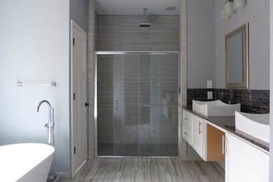 This is an example of a large contemporary master bathroom in Dallas with shaker cabinets, white cabinets, a freestanding tub, an alcove shower, gray tile, glass tile, grey walls, vinyl floors, a vessel sink, granite benchtops, beige floor and a sliding shower screen.