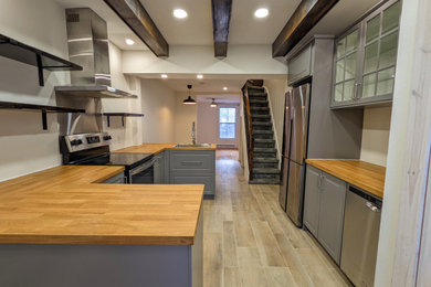 Example of a mid-sized country u-shaped laminate floor and beige floor kitchen design in Montreal with a drop-in sink, shaker cabinets, gray cabinets, wood countertops and stainless steel appliances