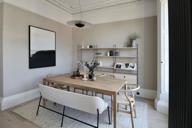Ejemplo de salón escandinavo grande con paredes beige, suelo de madera clara, estufa de leña, marco de chimenea de madera, televisor en una esquina y suelo beige