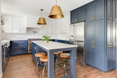 Photo of a medium sized traditional u-shaped open plan kitchen in Dallas with a belfast sink, shaker cabinets, blue cabinets, engineered stone countertops, white splashback, ceramic splashback, stainless steel appliances, porcelain flooring, an island, brown floors and white worktops.