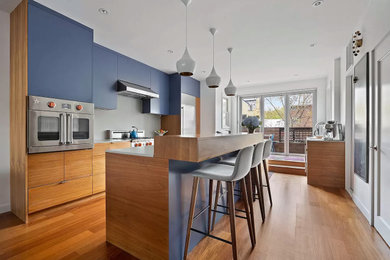 Open concept kitchen - mid-sized modern single-wall medium tone wood floor and brown floor open concept kitchen idea in New York with a single-bowl sink, flat-panel cabinets, medium tone wood cabinets, quartz countertops, gray backsplash, quartz backsplash, stainless steel appliances, an island and gray countertops