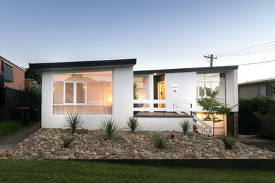 Inspiration for a midcentury one-storey stucco white house exterior in Canberra - Queanbeyan with a metal roof.