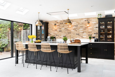 Large traditional single-wall kitchen/diner in London with a belfast sink, shaker cabinets, black cabinets, quartz worktops, black appliances, porcelain flooring, an island, grey floors, white worktops and a feature wall.