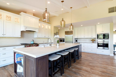 Inspiration for a large transitional l-shaped eat-in kitchen in Santa Barbara with a farmhouse sink, raised-panel cabinets, white cabinets, quartzite benchtops, beige splashback, glass tile splashback, stainless steel appliances, vinyl floors and with island.