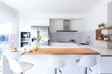Design ideas for a mid-sized contemporary u-shaped open plan kitchen in Barcelona with flat-panel cabinets, white cabinets, grey splashback, stainless steel appliances, a peninsula, white benchtop, an undermount sink and glass sheet splashback.